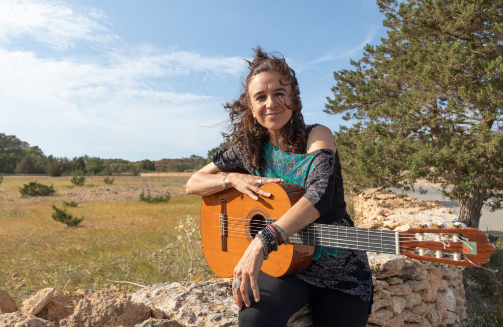 Portrait photo of Roxana Mouriño and her guitar in Formentera's countryside