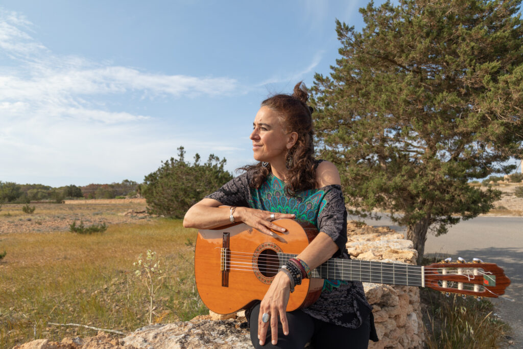 Portrait photo of Roxana Mouriño and her guitar in Formentera's countryside