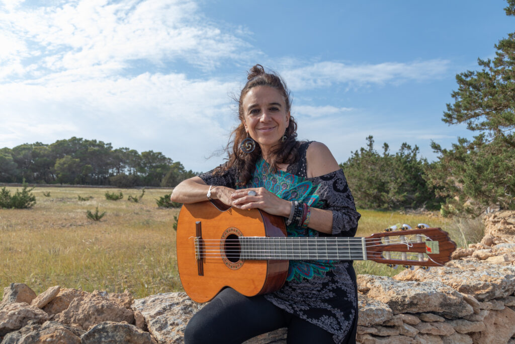 Portrait photo of Roxana Mouriño and her guitar in Formentera's countryside